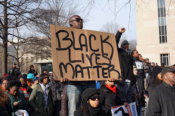 Black Lives Matter Washington DC, USA-December 13, 2014: This man is protesting police brutality at a protest led by Reverend Al Sharpton on Pennsylvania Avenue in Washington DC. He displays a sign with the message Black Lives Matter.  Recently the deaths of Michael Brown, Eric Garner and Tamir Rice have upset the black community. police brutality photos stock pictures, royalty-free photos & images