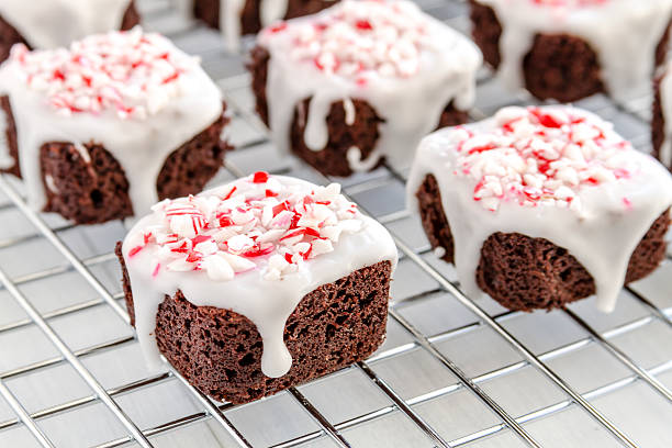 Chocolate Peppermint Brownie Bites Close up of chocolate brownie bites covered with white icing and candy cane sprinkles sitting on wire baking rack candy peppermint christmas mint stock pictures, royalty-free photos & images