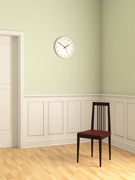 An elegant wooden chair with padded leather seat, standing under a wall clock in an empty room. Symbolic suggestion of isolation, sadness or departure.