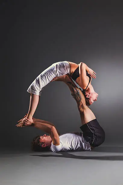 Couple practicing acro yoga against gray background