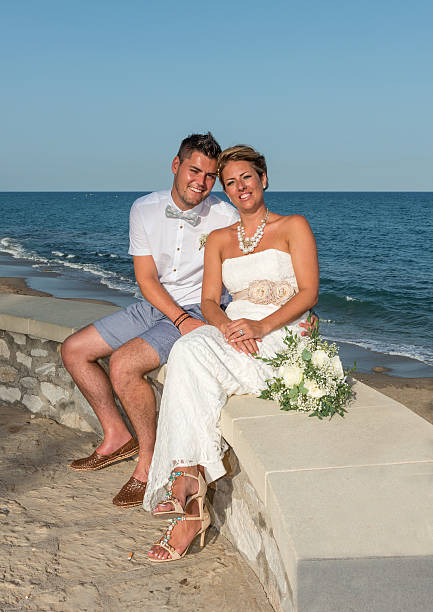 istock Bride and Groom sitting on wall next to the sea 528394053