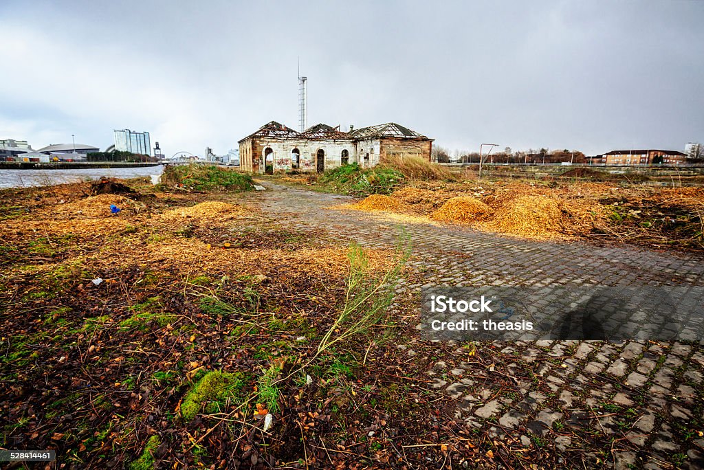 The Derelict Graving Docks at Govan, Glasgow Burnt out buildings amongst the overgrowth at the derelict Victorian graving docks - a type of dry dock - in Govan, Glasgow, on the River Clyde. In the background is the modern Glasgow skyline. Abandoned Stock Photo