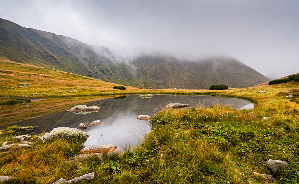 istock Small Tarn with Rocks in Foggy Mountains 528419962