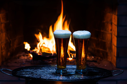 two beers with fireplace on background
