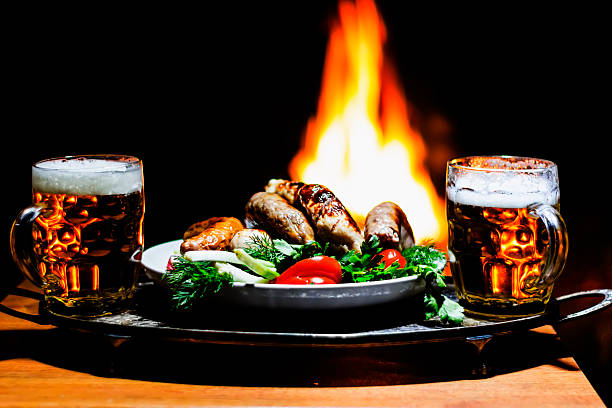 two beers and sausages with fireplace on background