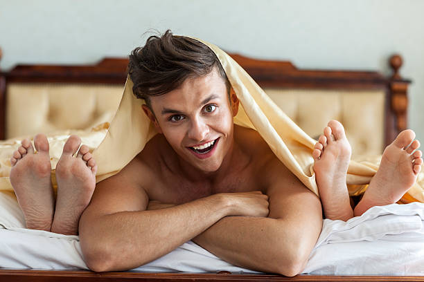 Man In Bed With Two Women Smiling man covered with blanket, lying in bed between feet of two women in a hotel room. menage trois stock pictures, royalty-free photos & images