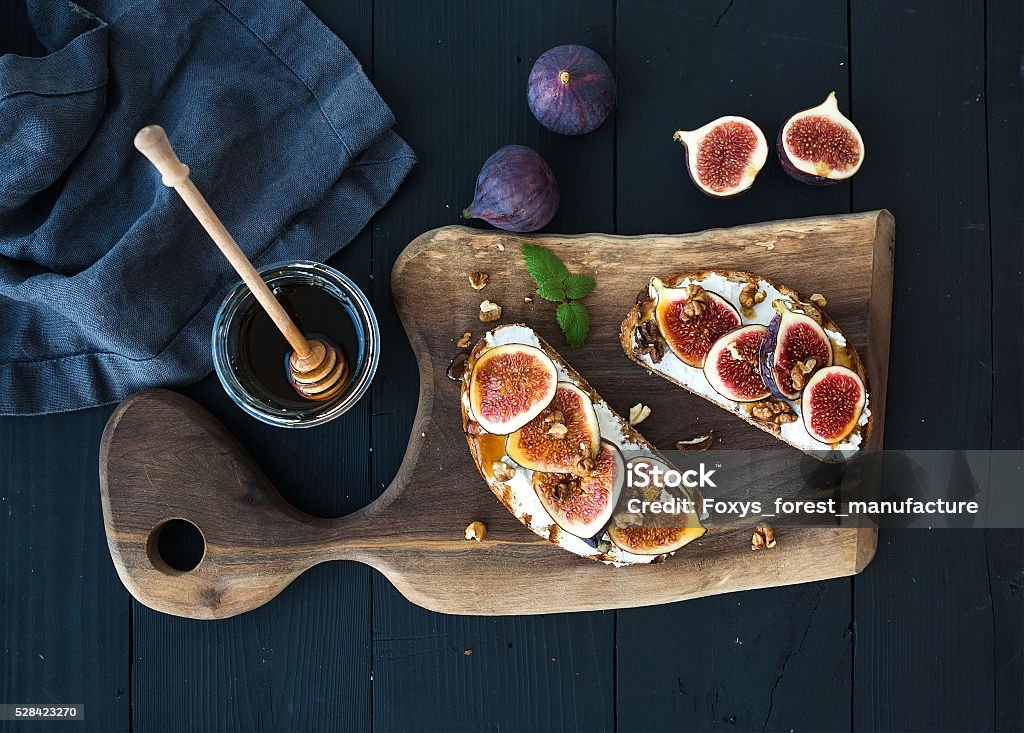 Sandwiches with ricotta, fresh figs, walnuts and honey on rustic Sandwiches with ricotta, fresh figs, walnuts and honey on rustic wooden board over black backdrop, top view Fig Stock Photo