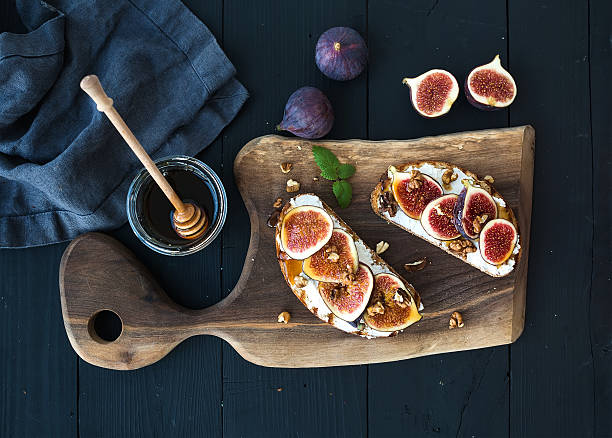 Sandwiches with ricotta, fresh figs, walnuts and honey on rustic Sandwiches with ricotta, fresh figs, walnuts and honey on rustic wooden board over black backdrop, top view crostini photos stock pictures, royalty-free photos & images