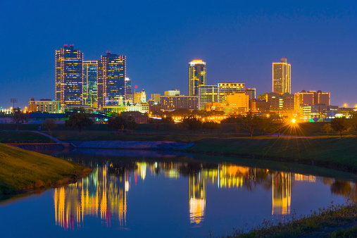 Fort Worth skyline at dusk / early evening, with the Trinity River in the foreground.