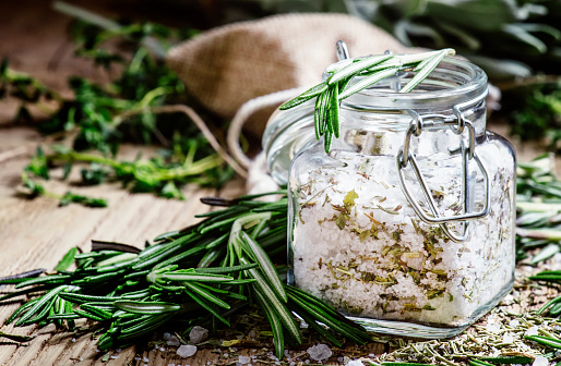 Sea salt with dried rosemary in a glass jar, vintage wooden background, selective focus