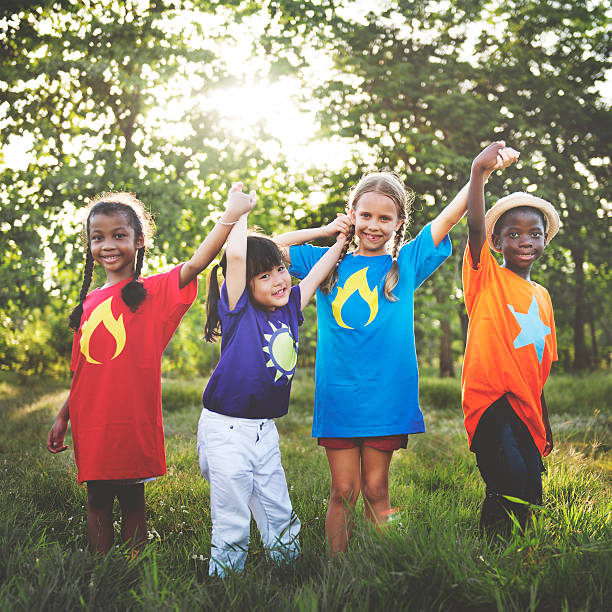 Group of multi-ethnic kids holding hands, on grass hill with blue sky