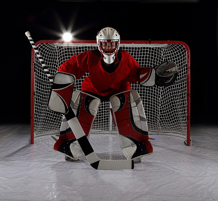 A young female ice hockey goalie guards the net.