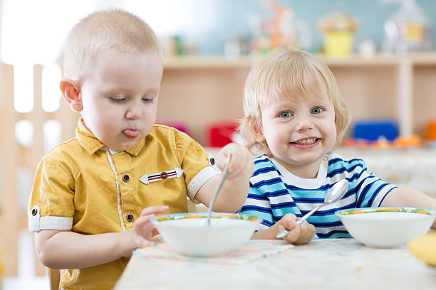 istock Two funny smiling little kids eating in kindergarten 528429852