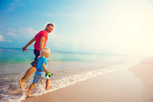 Father And Son Running Along Beach stock photo