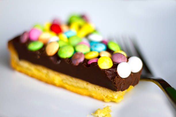 Fancy pasty slice with colorful candy-coated chocolate bits, with crumbs. White plate background with fork. Copy space available.
