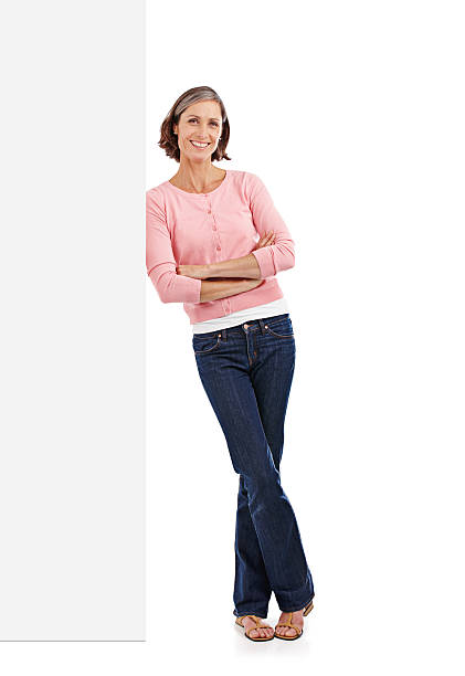 Laid-back style Full-length studio shot of an attractive mature woman leaning against a blank white sign leaning stock pictures, royalty-free photos & images