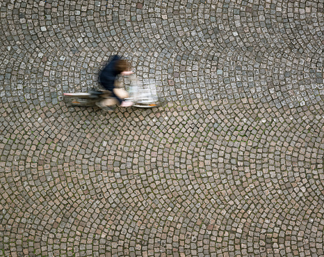 Motion blur on a cyclist as he rides over old-fashioned, patterned cobbles in Montparnasse, Paris.  Photographed from directly above.