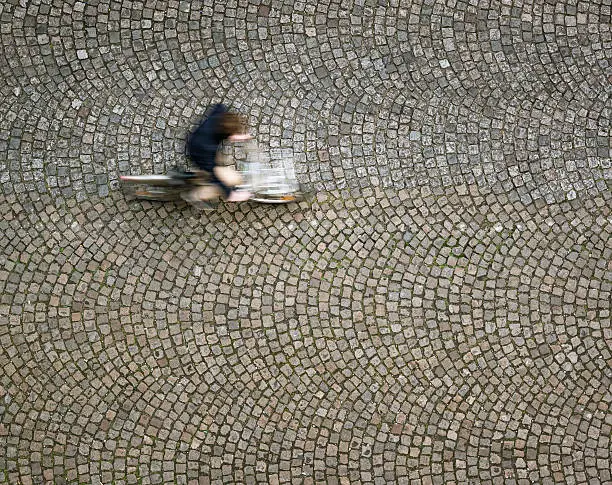 Motion blur on a cyclist as he rides over old-fashioned, patterned cobbles in Montparnasse, Paris.  Photographed from directly above.