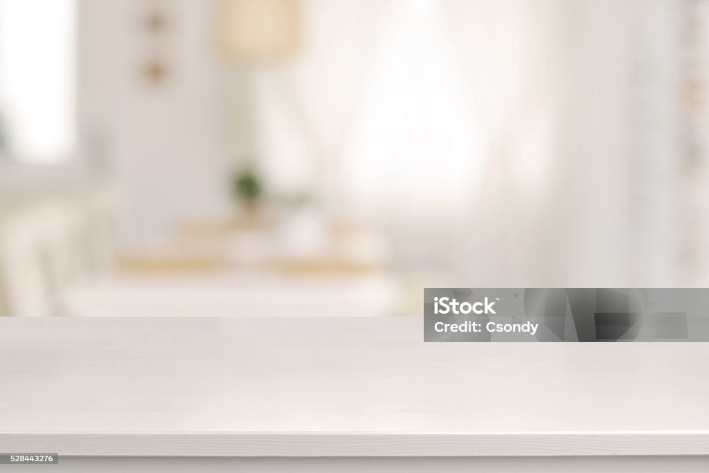 White wooden table and blurred dining room Empty white wooden table and blurred dining room interior decoration background. Product display. Sun is shining trhough the window. Table Stock Photo