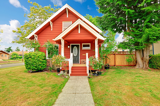 Small coutnryside house exterior in bright red color with white trim. Entrance porch with stairs and white railings