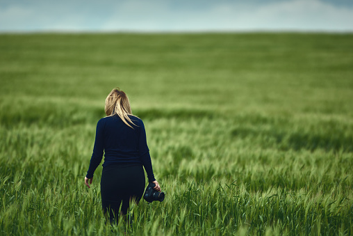 rear view of photographer woman walking in green field, preparing for nature shot.