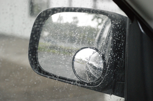 The view from a motor vehicle side mirror through the window in the rain. The image layers up due to the blind spot mirror giving a different angle of view.