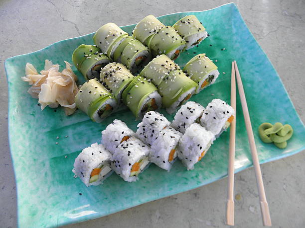 Sushi - 3 vegetarian Inside-out rolls (algae in rice on the outside) with vegetables (avocado, carrot, cucumber, shiitake mushrooms, sweet potato), sprinkled with sesame seeds. Served on a blue plate with ginger and wasabi. Asian, Japanese, vegetarian, vegan food.