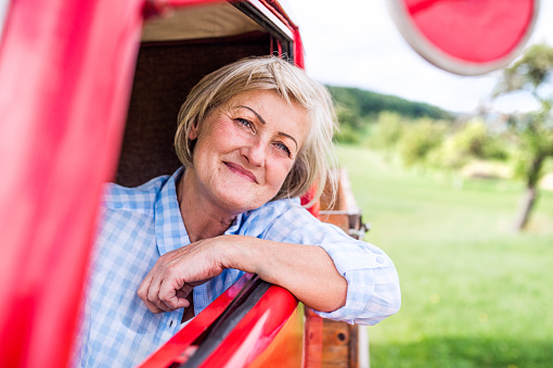Close up of senior woman in checked blue shirt inside vintage pickup truck
