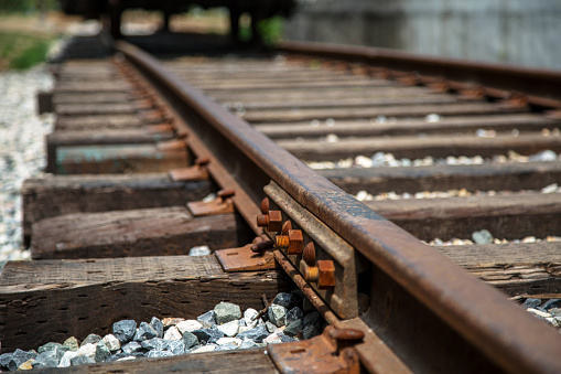 Selective focus railway track turns and twists between hills. Empty rounding and turning single track of railways. Shallow focus perspective view of rounded rails bend horizontal, 16x9.