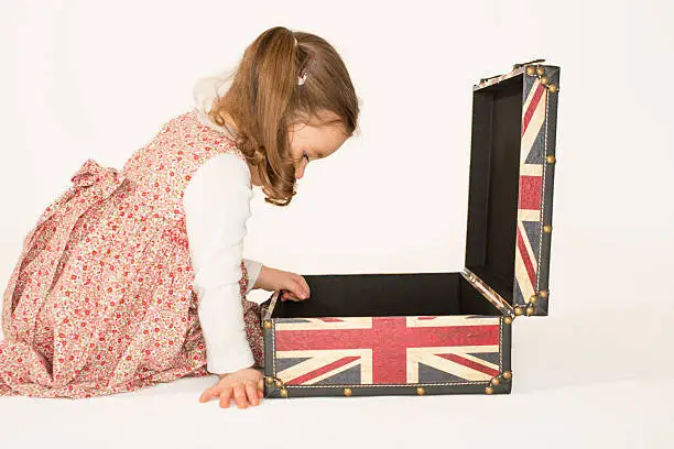 Beautiful little girl looking inside old style suitcase with British flag on it, studio shot on white background