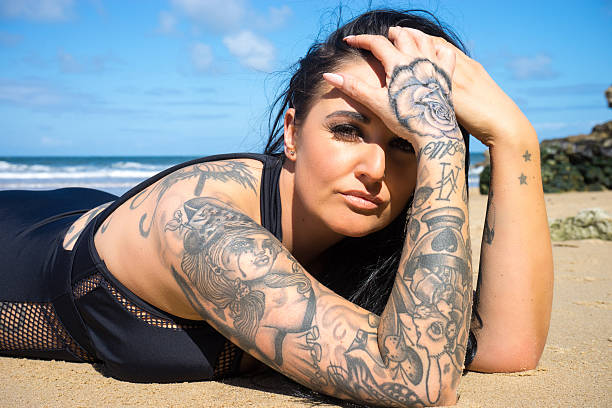 wytatuowany kobieta leżący na piaszczysta plaża - tattoo sleeve zdjęcia i obrazy z banku zdjęć