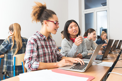 Group of female students coding on laptops in a computer lab. Close up of asian and afro american young women discussing.