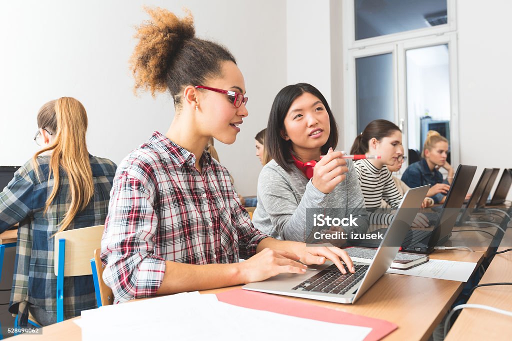 Female students learning computer programming Group of female students coding on laptops in a computer lab. Close up of asian and afro american young women discussing. Classroom Stock Photo