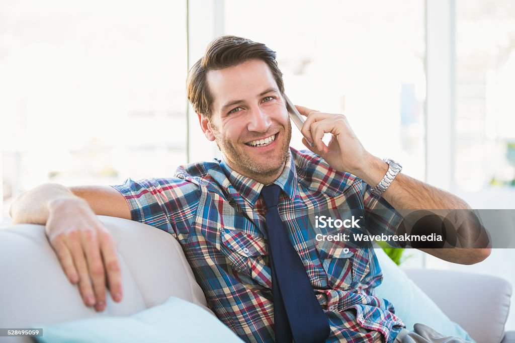 Cheerful man sitting on the couch making a phone call Cheerful man sitting on the couch making a phone call in bright living room 30-34 Years Stock Photo