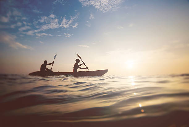 couple on a boat silhouette of a couple on a boat in the sea at sunset kayaking stock pictures, royalty-free photos & images