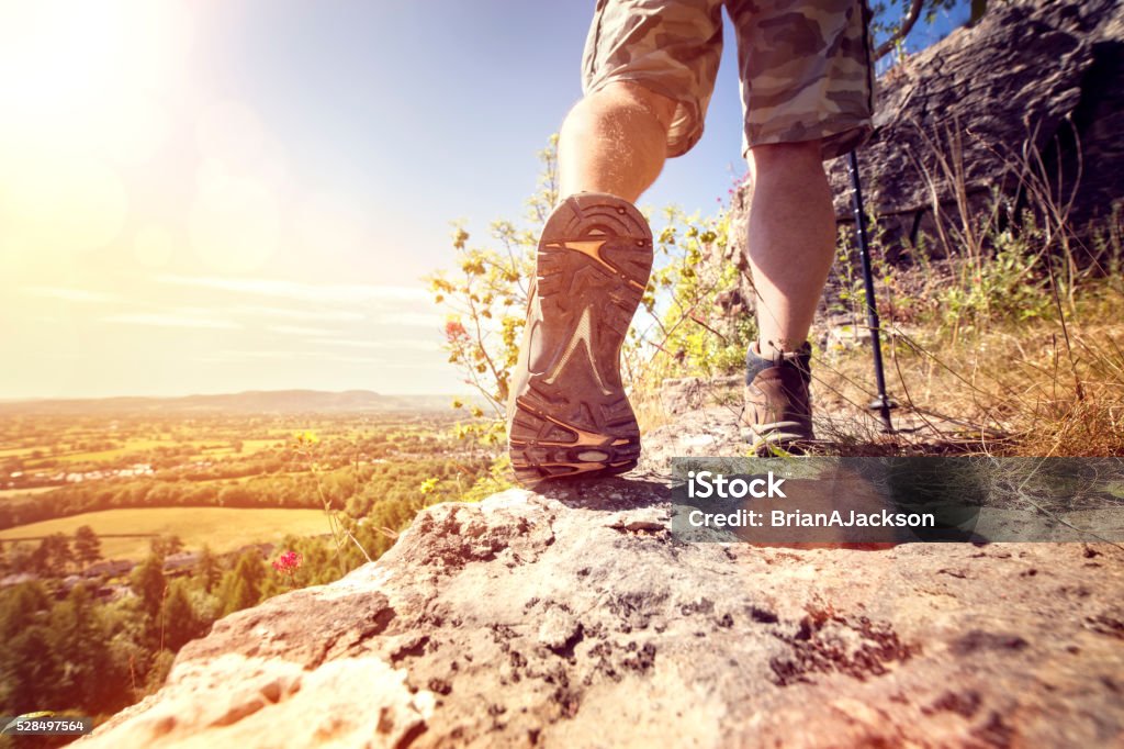 Hiking on a mountain trail Hiker hiking on a mountain trail with distant views of countryside in summer sunshine Active Lifestyle Stock Photo