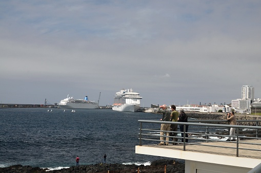 Ponta Delgado, portugal - April 24, 2016: Four birders, two from Germany, one American and a local Portuguese guide gather at the sewage treatment plant on Sao Miguel island overlooking the harbor with two large cruise ships docked. Two local fisherman are trying to catch fish at this nutrient rich location. The ship on the right is the Regal Princess, the ship on the left is unidentifiable. Tourist are also seen in the small sailboat dinghies being towed back to the ship after an excursion