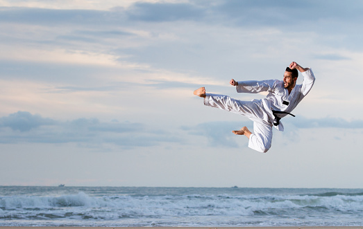 Young adult man with black belt jumping to practice Marcial Arts kick on the beach. Real shot, not a photomontage.