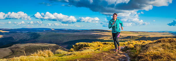 istock Young woman trail running over wilderness mountain ridge path panorama 528502646