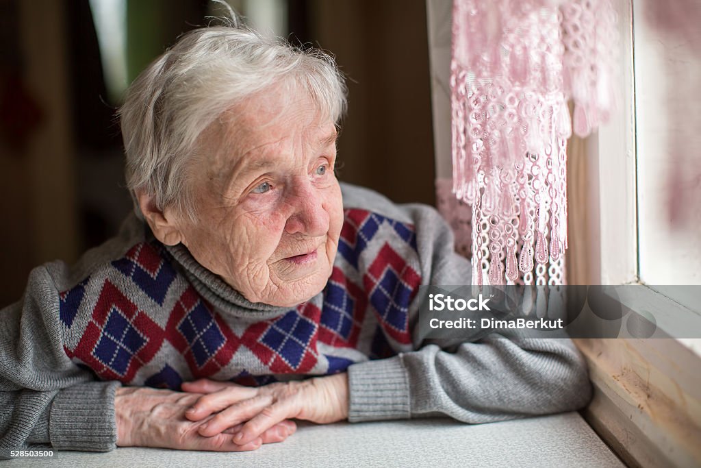 An elderly woman sits and looking out the window. Dementia Stock Photo