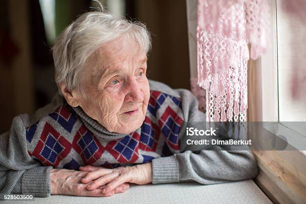 An Elderly Woman Sits And Looking Out The Window Stock Photo - Download Image Now - Dementia, Adult, Camera - Photographic Equipment