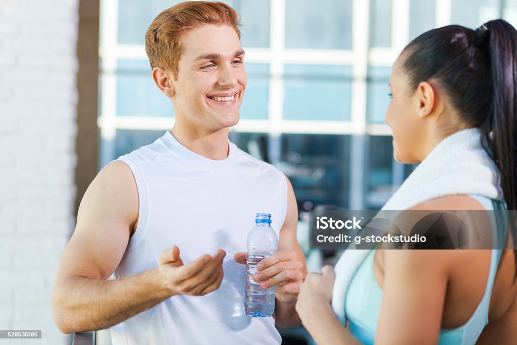 Relaxing after work out. Beautiful young sporty couple talking and smiling while standing in gym Adult Stock Photo