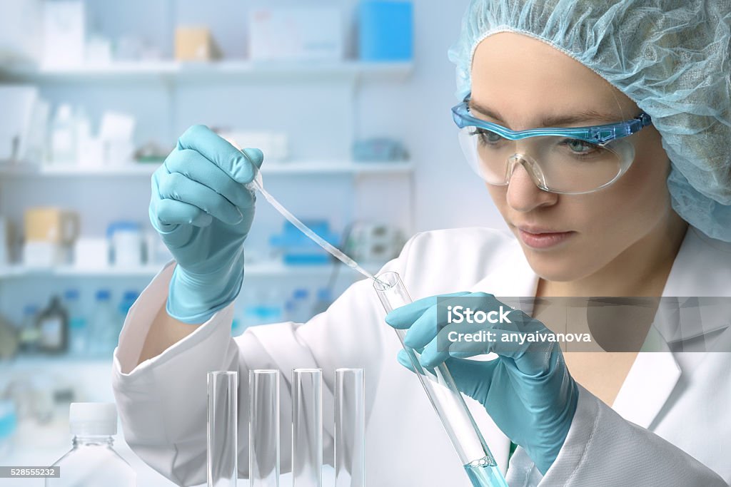 Young female tech or scientist performs protein assay Young female tech or scientist loads liquid sample into test tube with plastic pipette. Shallow DOF, focus on the hand with the tube. Laboratory Stock Photo