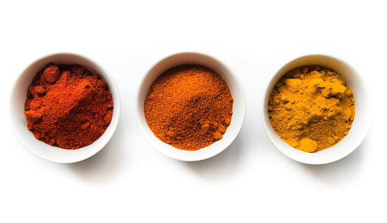Turmeric, cayenne, and paprika spice powders in white bowls on a white background