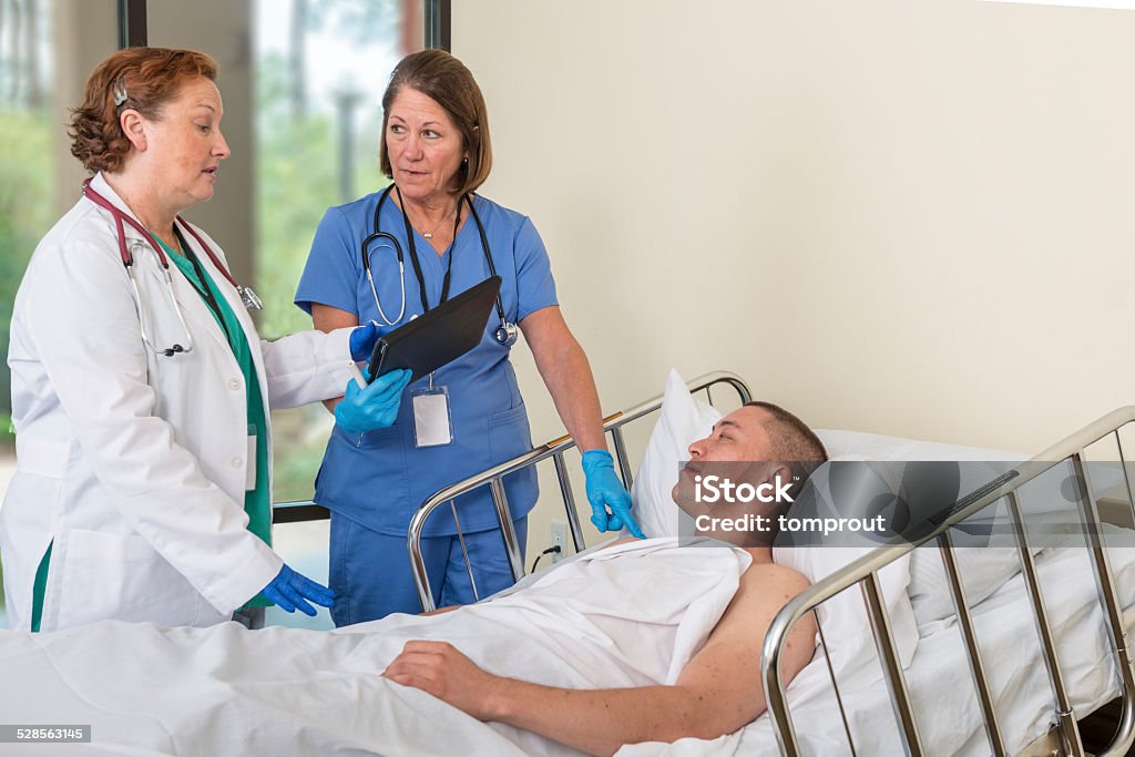 Doctor and Nurse Visiting Patient A doctor and nurse are making their rounds and visiting a patient. Bed - Furniture Stock Photo