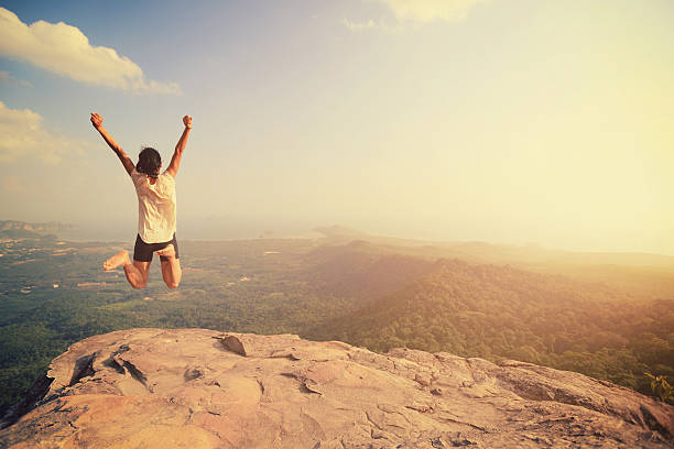 cheering young asian woman jumping on mountain peak rock