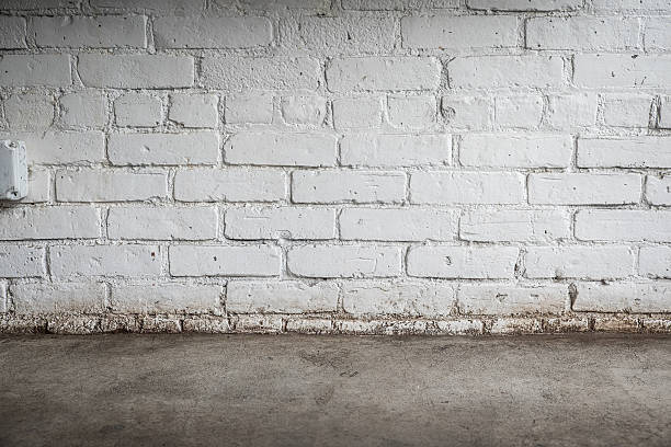istock Grungy Painted White Brick Wall with Concrete Floor 528568012