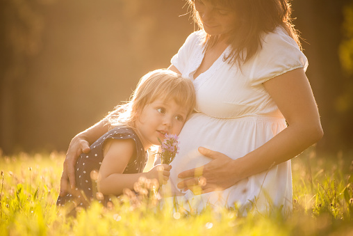 Little child listening baby in belly of her mother outdoor in sunny nature