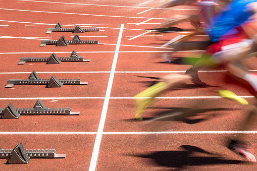 A side shot of a diverse group of females training on a running track. It is a bright day with blue skies. There are no spectators in the frame.