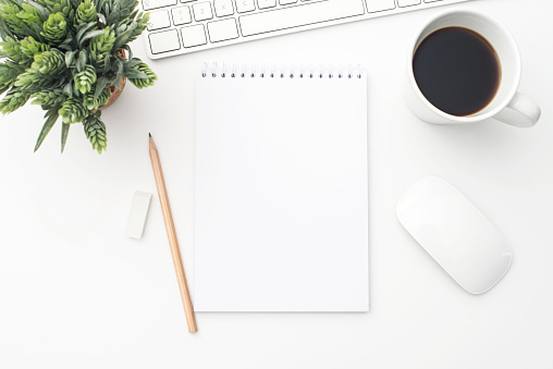 Modern office desk table with notebook and other supplies with cup of coffee. Blank notebook page for you design. Top view, flat lay.